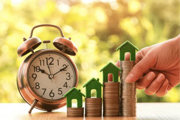 jardin-valorisation-patrimonial Épargne et investissement immobilier représentés par des pièces empilées, des maisons et une horloge