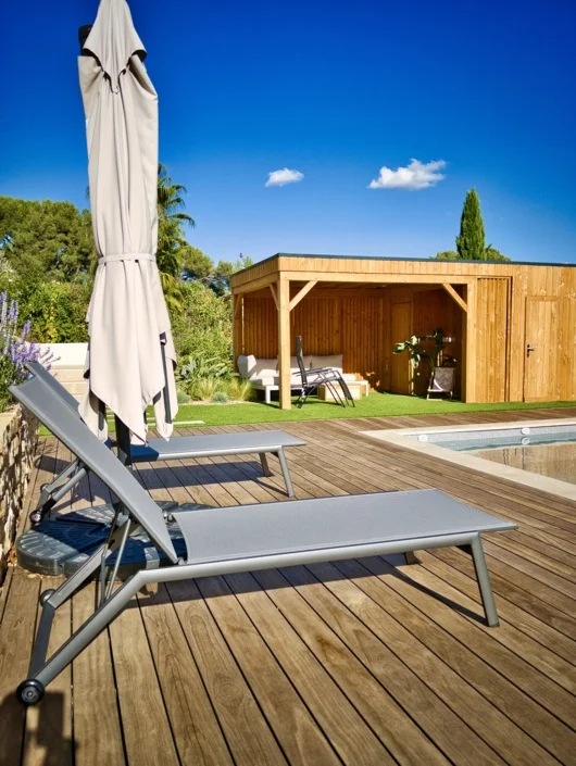 Plage de piscine en bois avec transats et pool house dans un jardin aménagé à Marseille